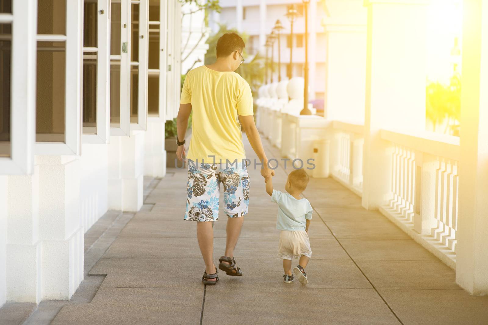 Back view of father and son holding hands walking in sunset. Parent and toddler on vacation.