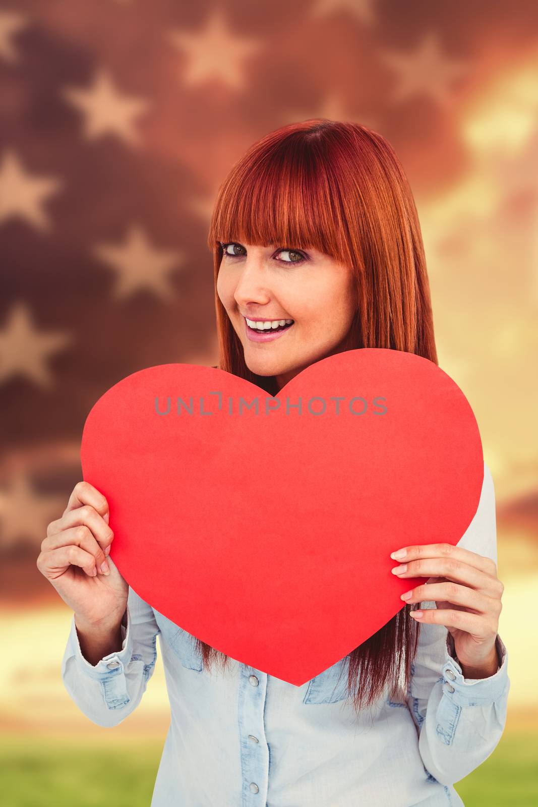 Attractive hipster woman behind a red heart against american flag rippling over grassy landscape