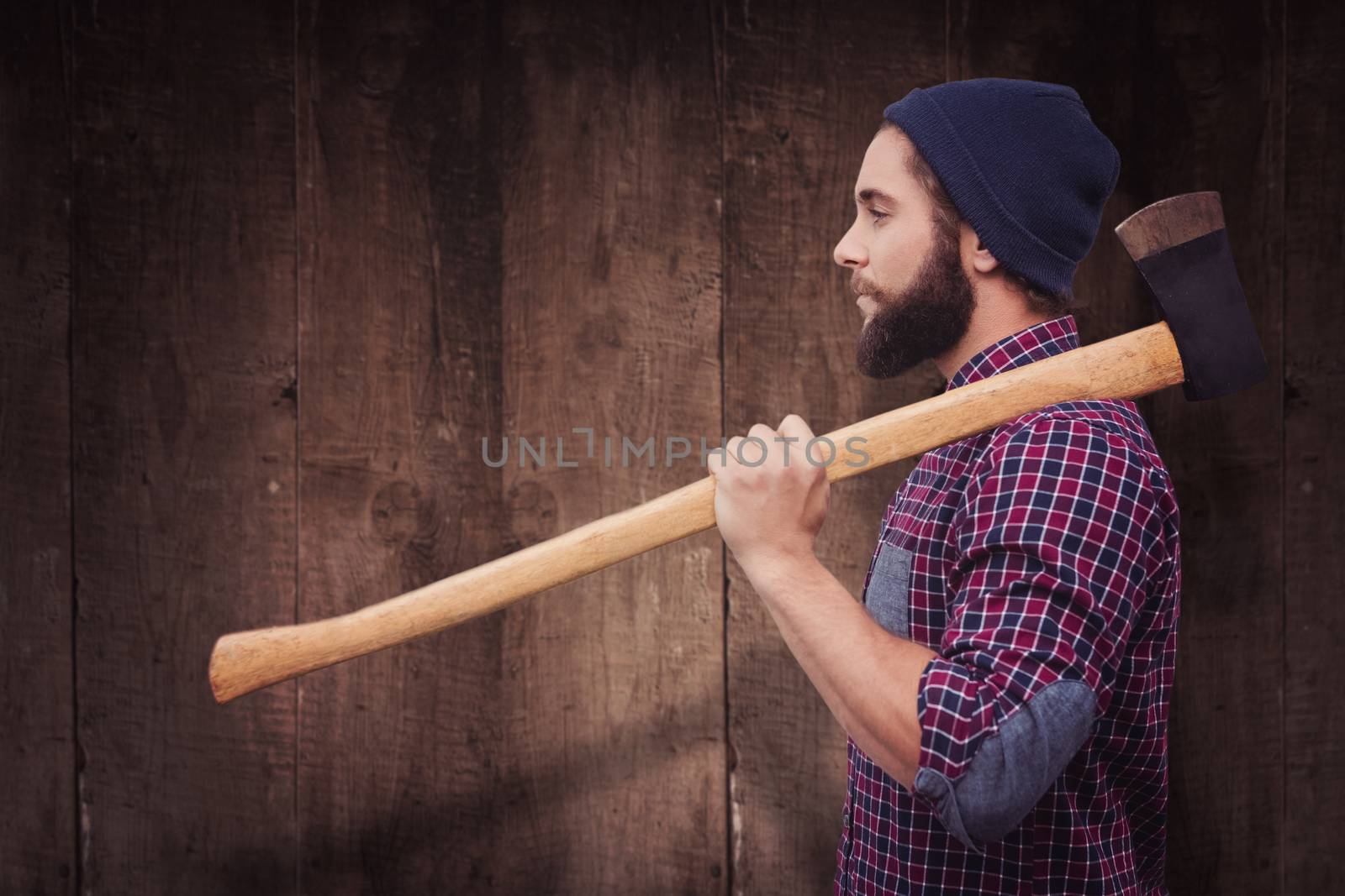 Side view of hipster with axe on shoulder against weathered oak floor boards background