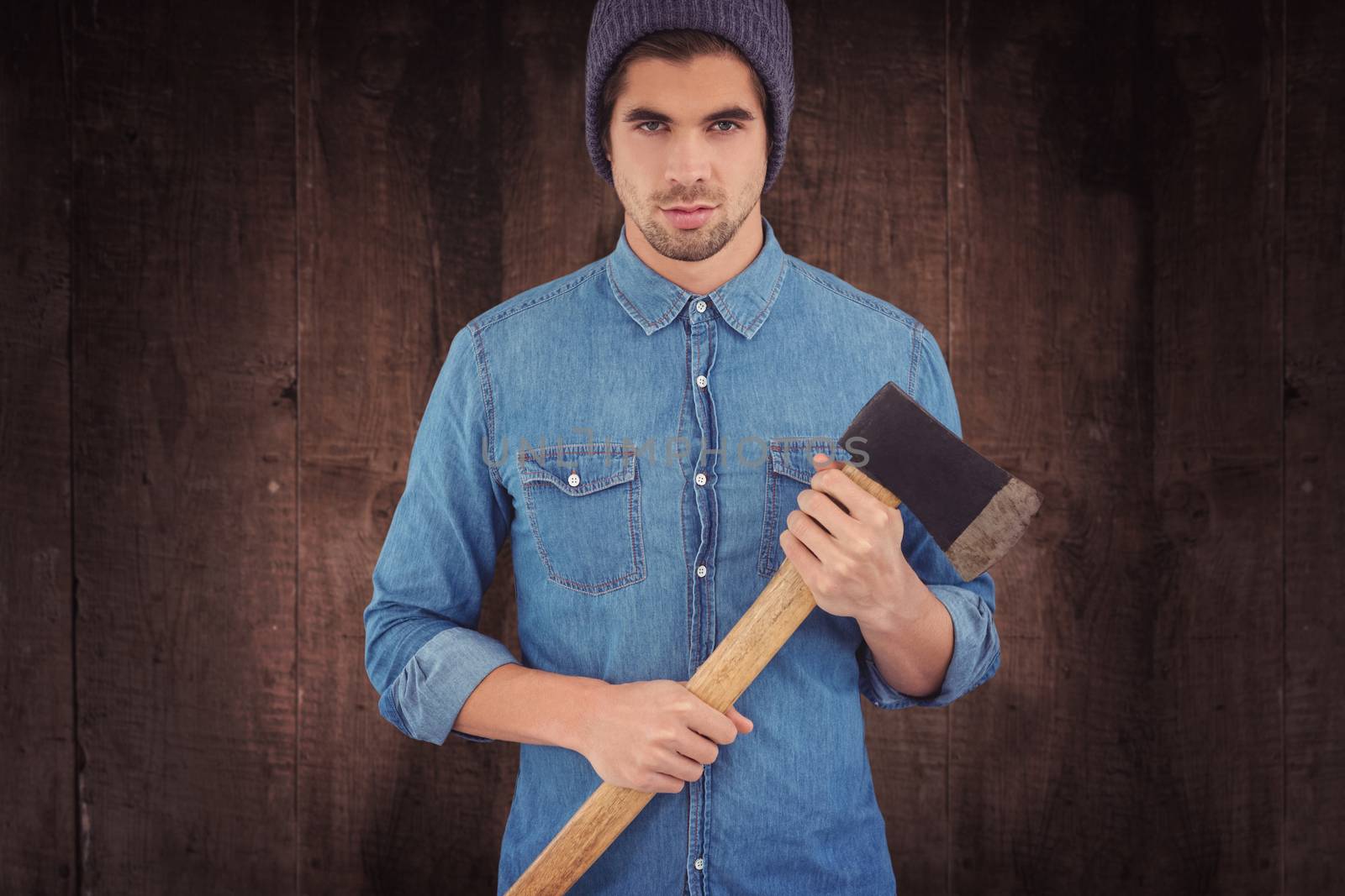 Serious hipster wearing knitted hat holding axe against weathered oak floor boards background