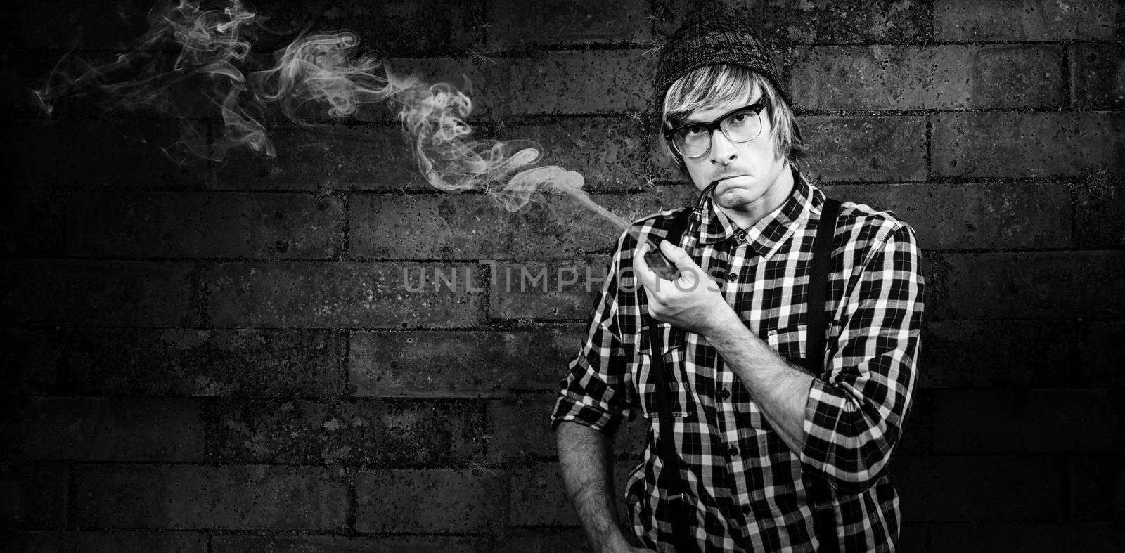Serious blond hipster smoking a pipe against texture of bricks wall