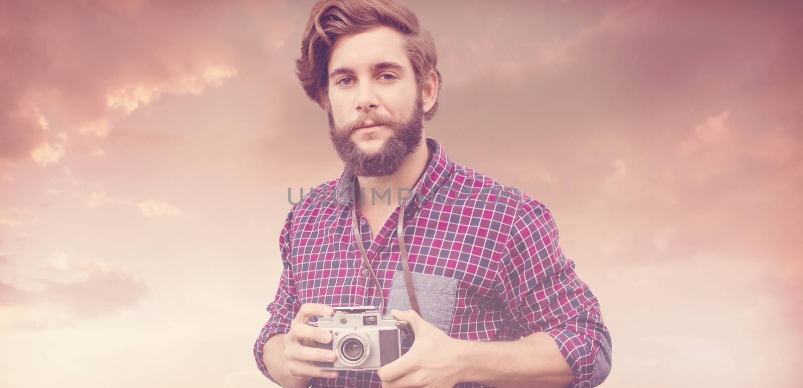 Portrait of confident hipster using camera against blue and orange sky with clouds