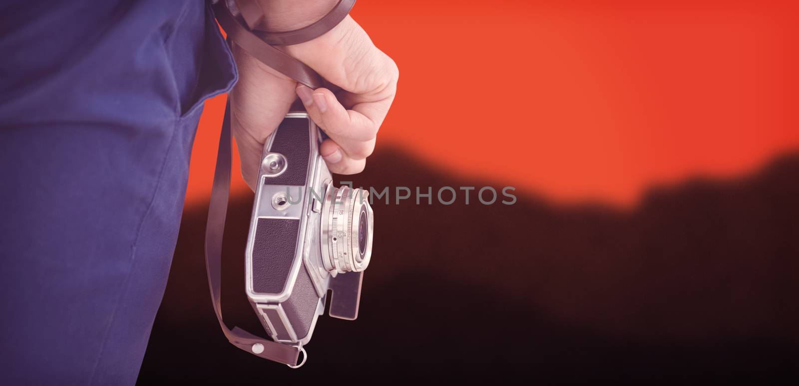 Cropped image of hipster holding camera against blurred mountains