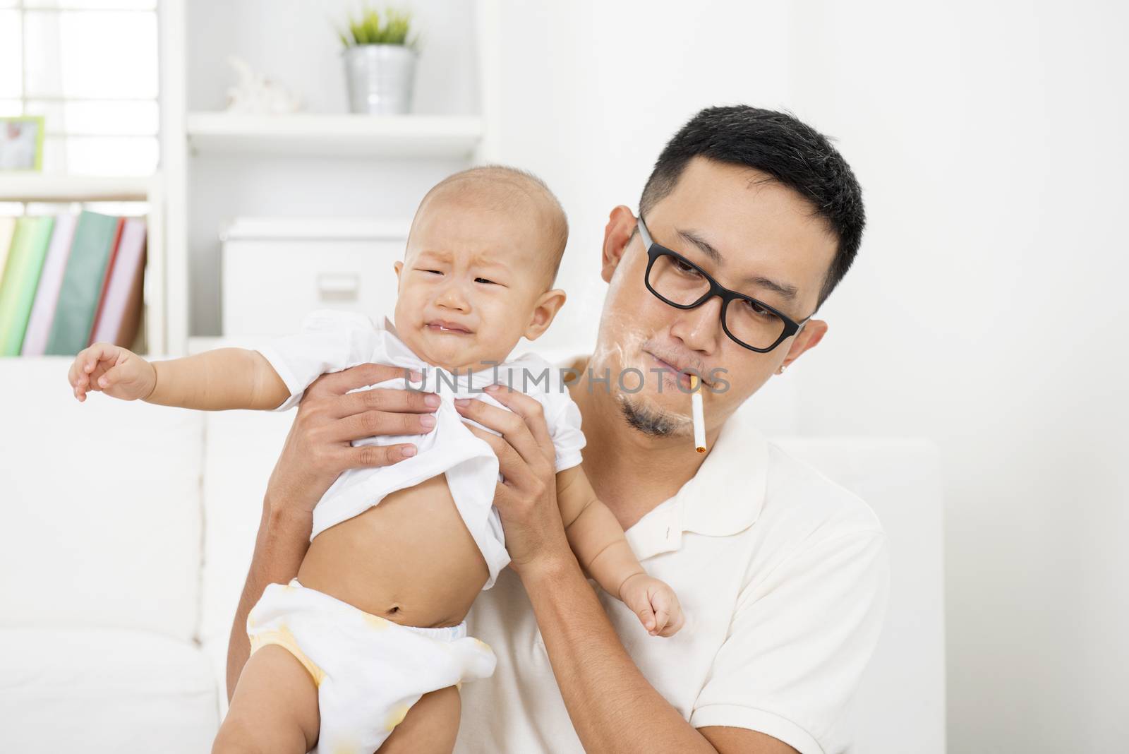Asian family at home. Bad father smoking while holding baby together. Cigarette with lit and smoke. Unhealthy lifestyle or stop smoking concept photo.