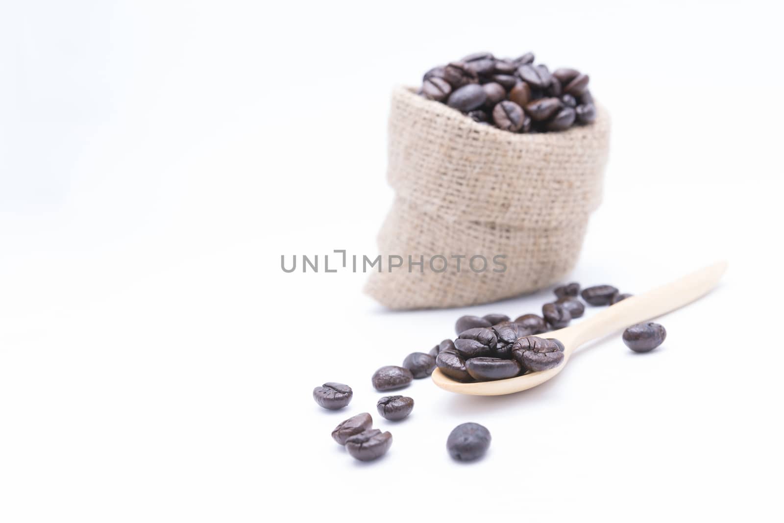 Coffee beans in a wooden scoop and spilling out from a hessian bag, over white background.