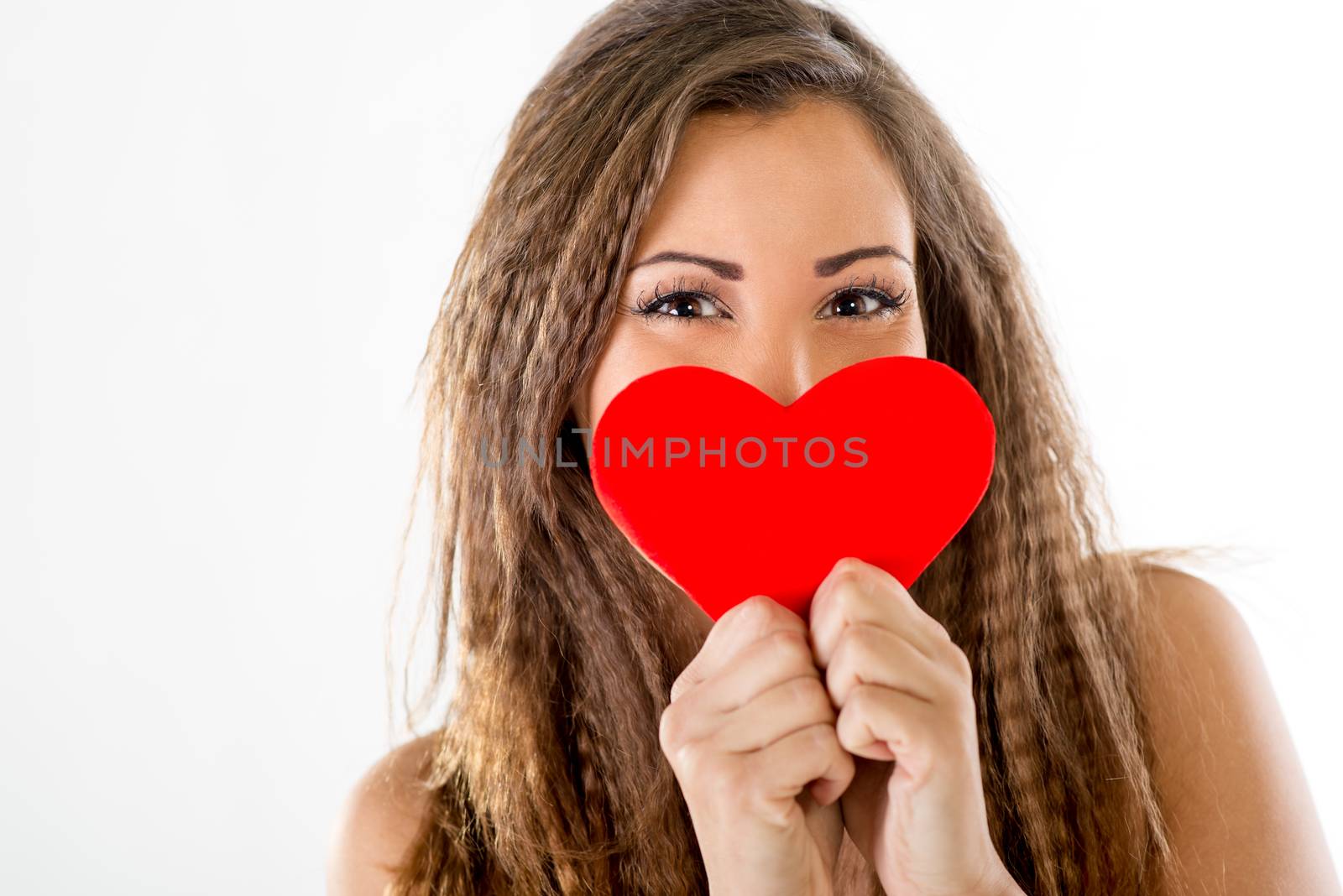 Beautiful smiling girl hiding behind a red heart. Looking at camera.