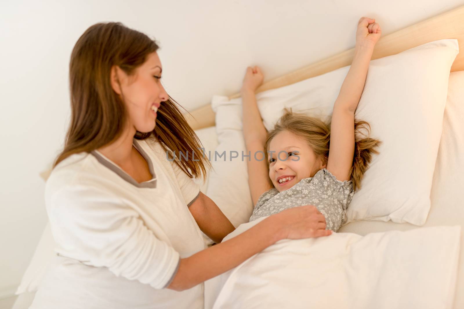 Happy attentive mother waking up her daughter at morning.