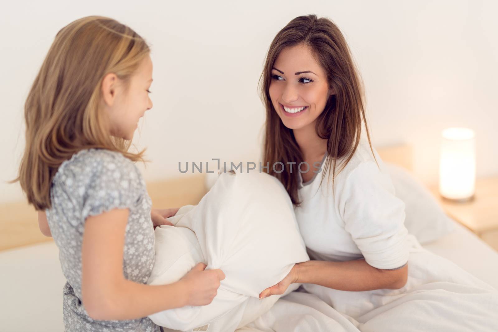 Beautiful smiling mother and her daughter having fun in bed.