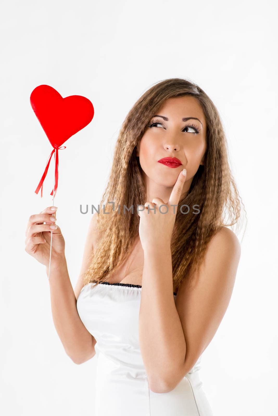 Beautiful thinking girl standing and holding red heart. 