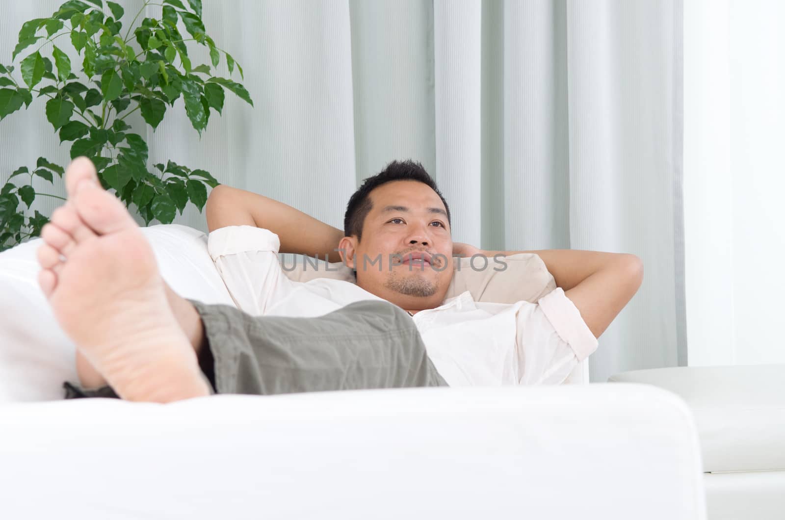 May guy resting and daydreaming at home. Asian handsome man relaxed and lying on sofa indoor. 
