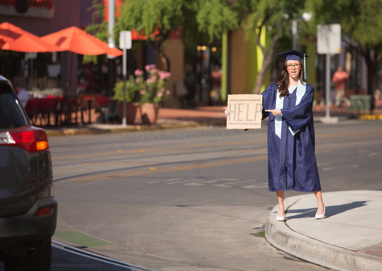 College graduate standing in street with help sign