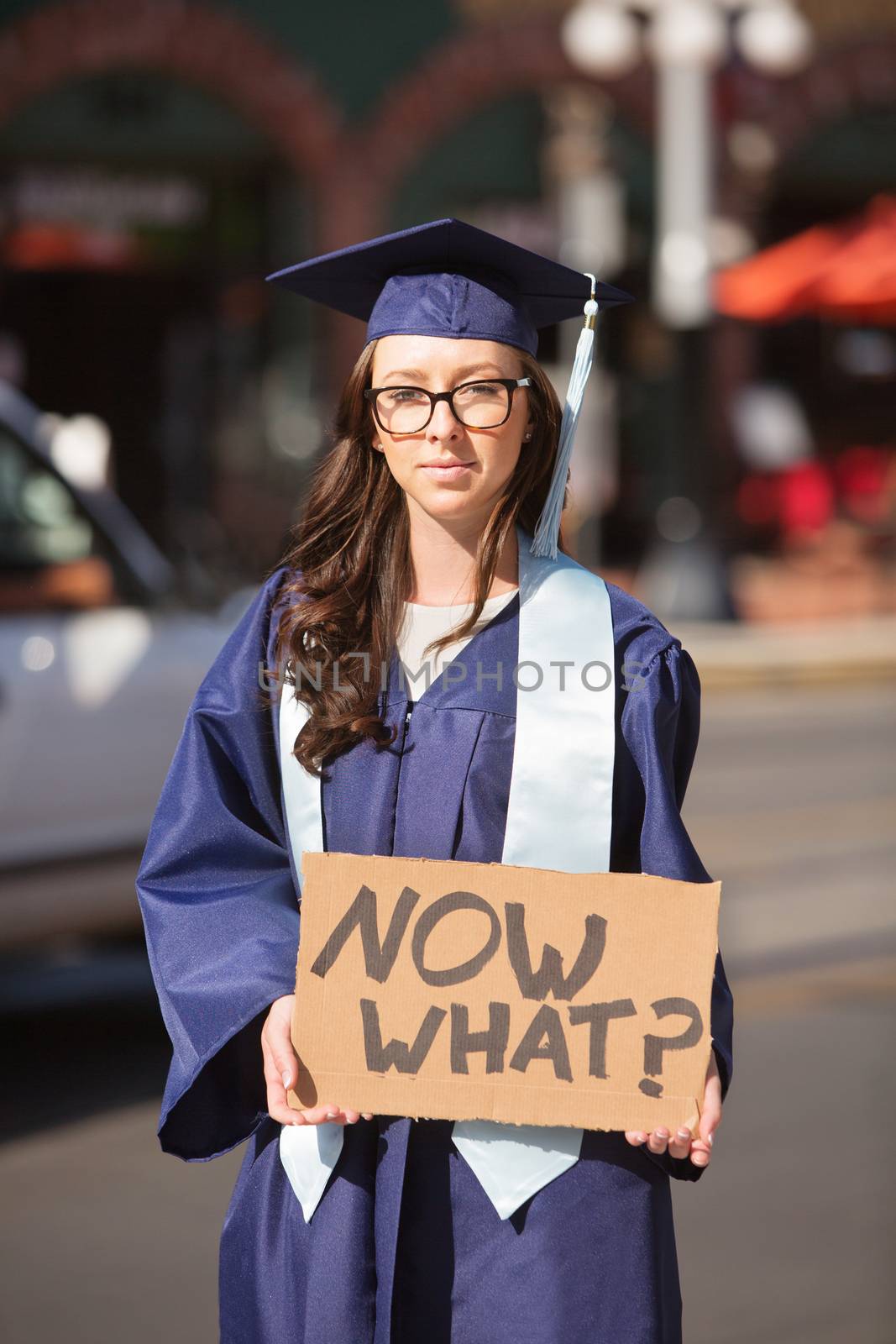 Uncertain college graduate in blue holding cardboard sign