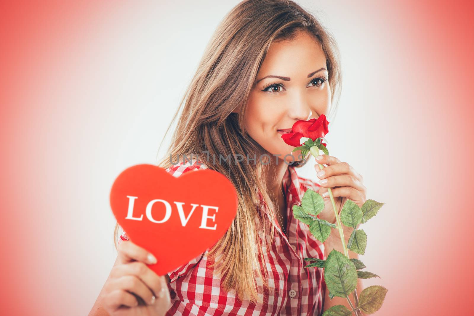 Portrait of a beautiful smiling girl holding a red heart and rose. Looking at camera.