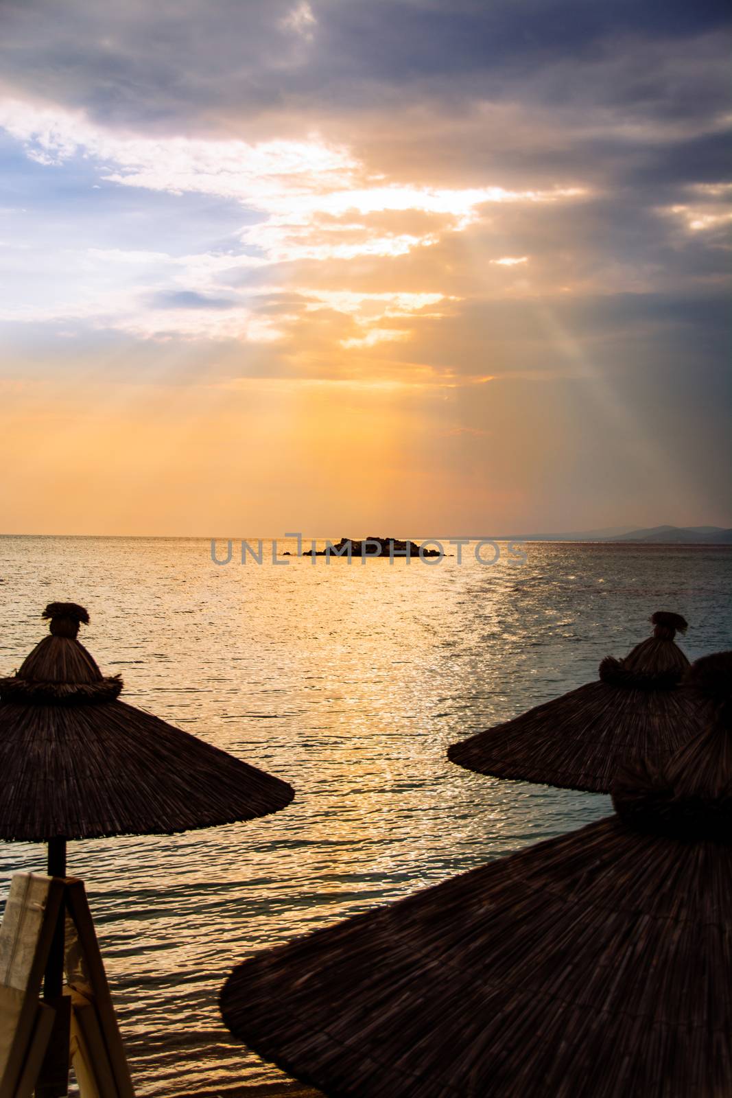 Beautiful sea sunset above silhouette of a beach umbrellas. 