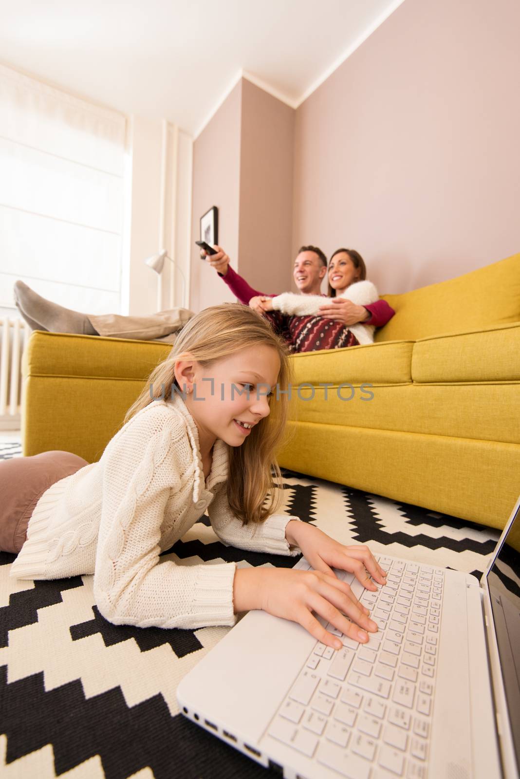 Beautiful young family enjoying a leisure activity at home. Little girl using a laptop, parent watching a tv. Selectiv focus.