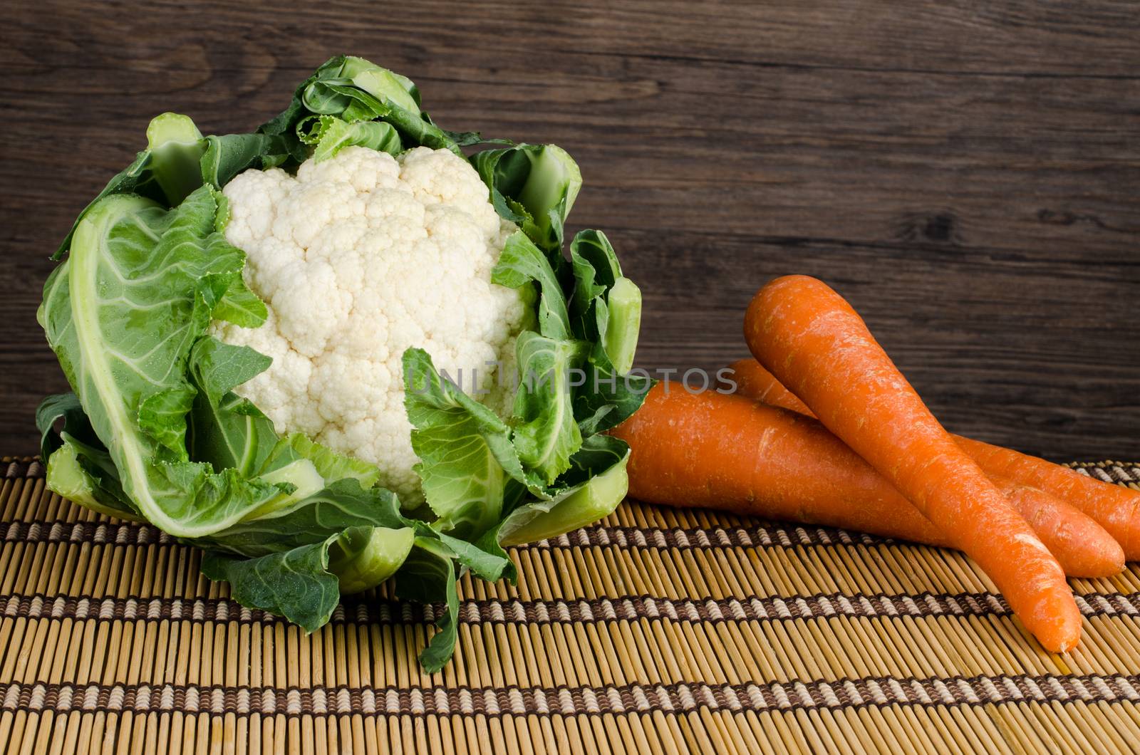 Fresh carrot  and cauliflower on straw palcemat and wooden background