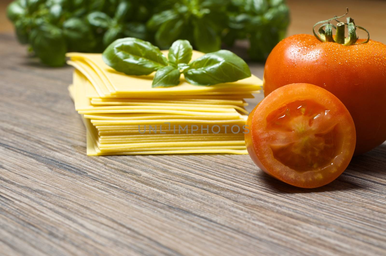 Raw pasta lasagna with basil leaves and fresh tomatoes on wooden background