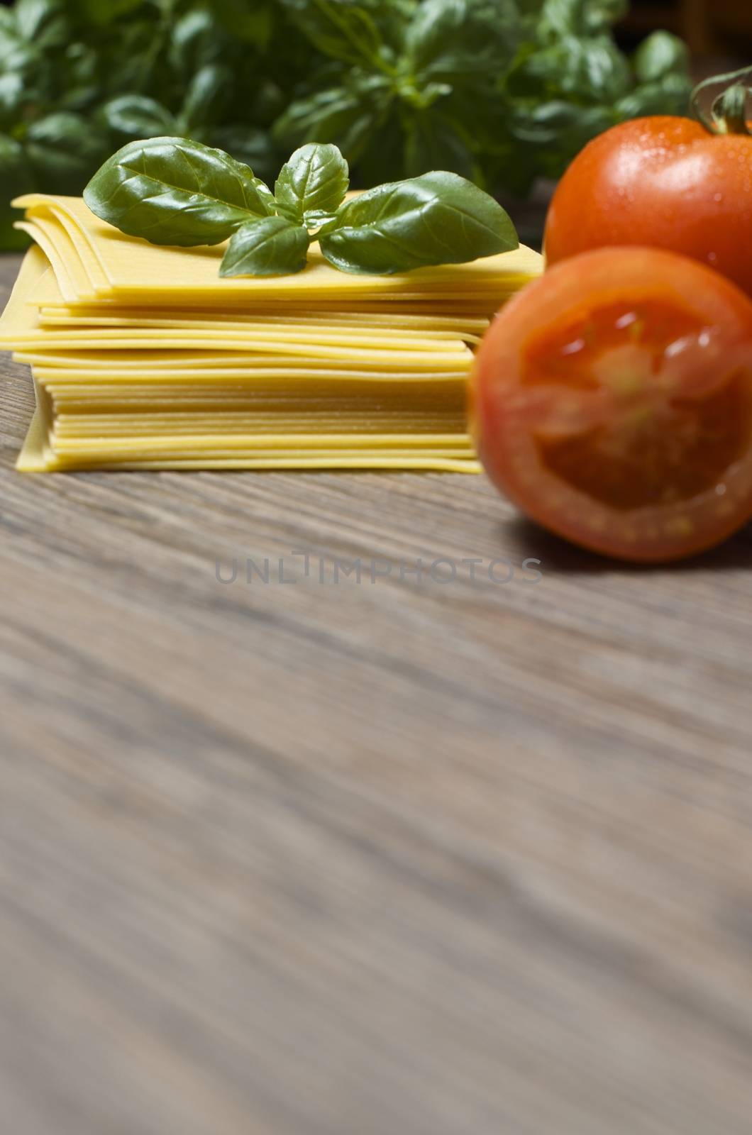 Raw pasta lasagna with basil leaves and fresh tomatoes on wooden background