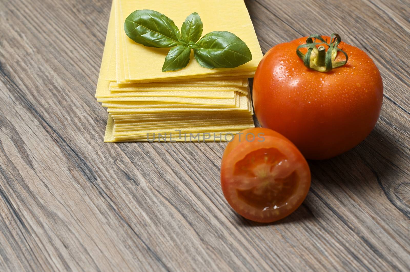 Raw pasta lasagna with basil leaves and fresh tomatoes on wooden background