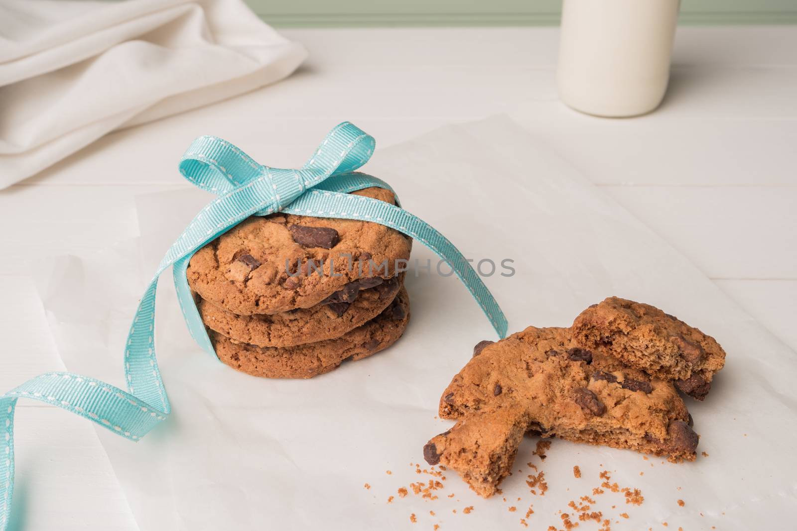 Chocolate chip cookies with a blue ribbon and a glass of milk on a white wooden table with a robin egg blue background. Vintage look.