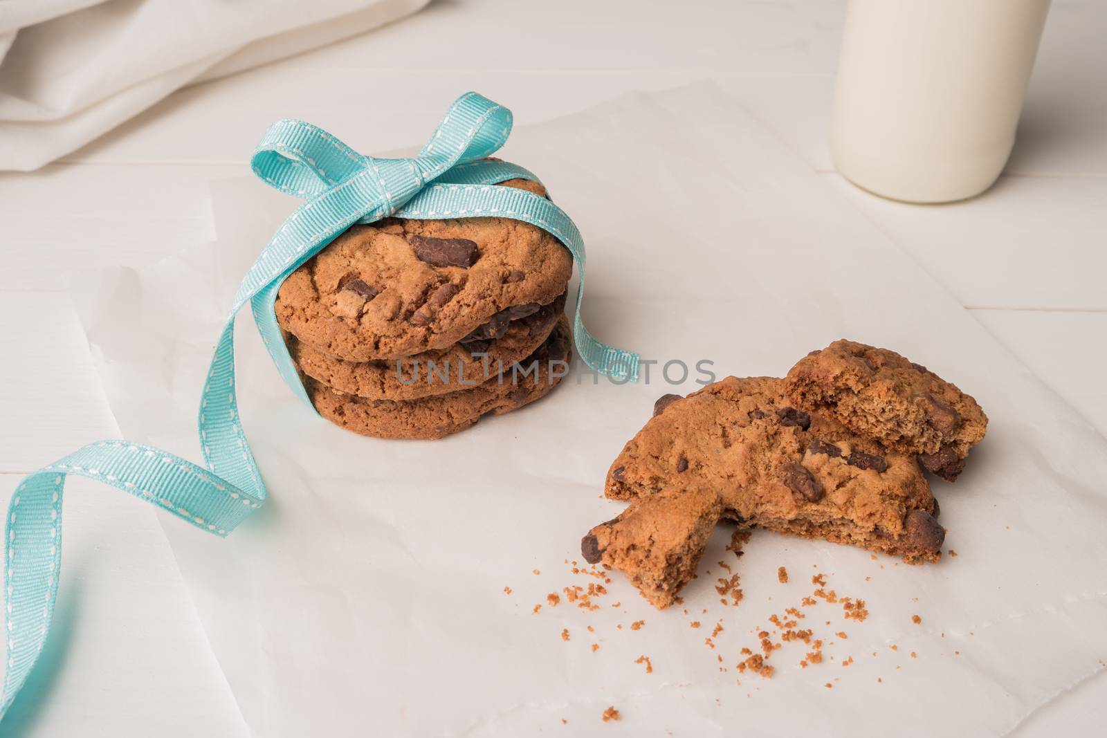 Chocolate chip cookies with a blue ribbon and a glass of milk on a white wooden table background. Vintage look.