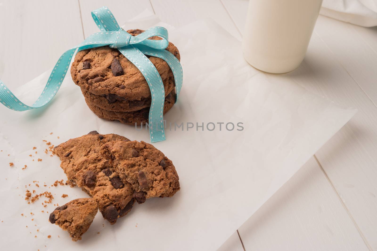 Chocolate chip cookies with a blue ribbon and a glass of milk on a white wooden table background. Vintage look.