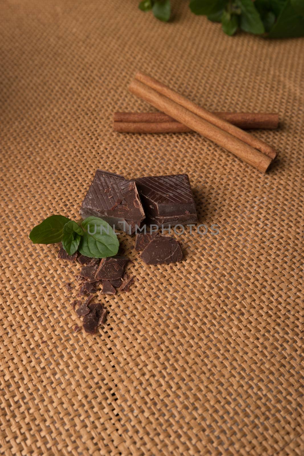 Broken chocolate bar and cinammom and mint leaf on placemat.