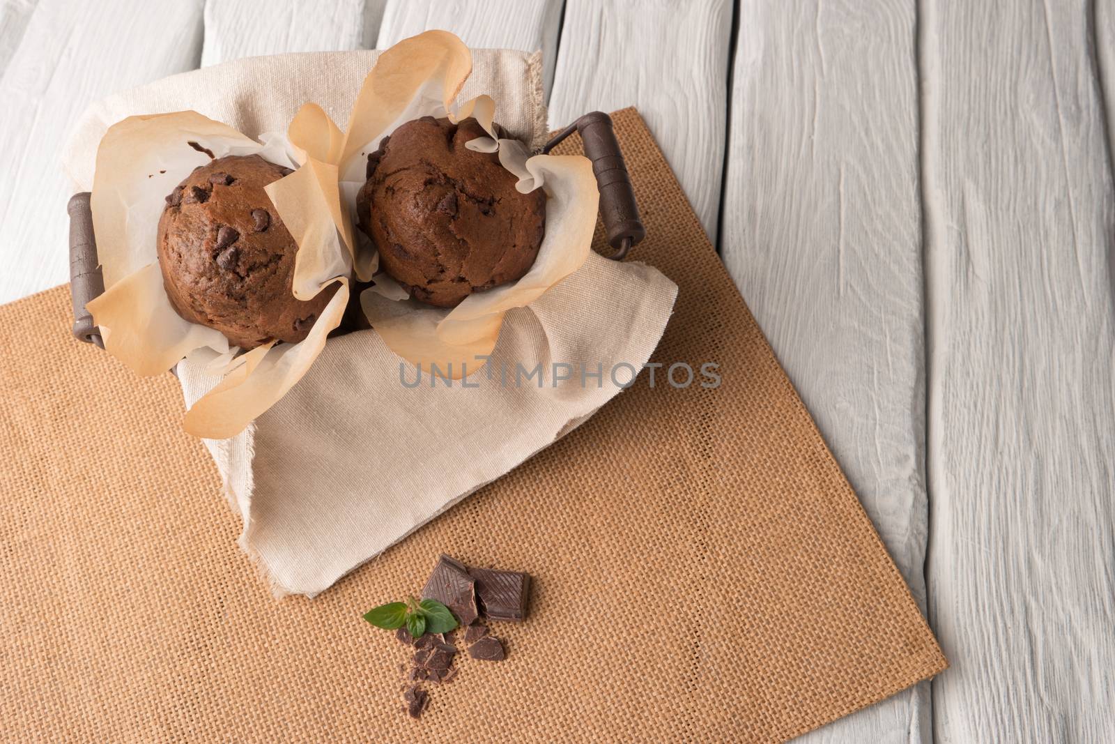 Chocolate muffins with chocolate slices in basket, cinnamom sticks and mint on placemat