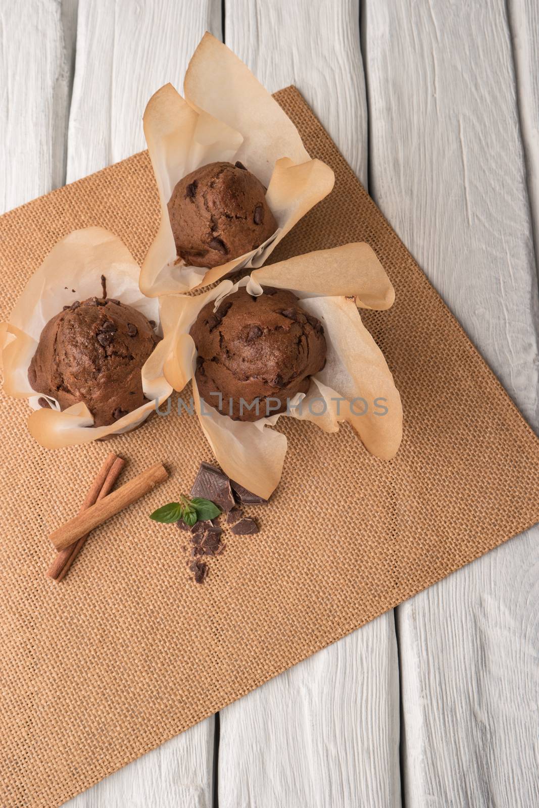 Chocolate muffins with chocolate slices in basket, cinnamom sticks and mint on placemat