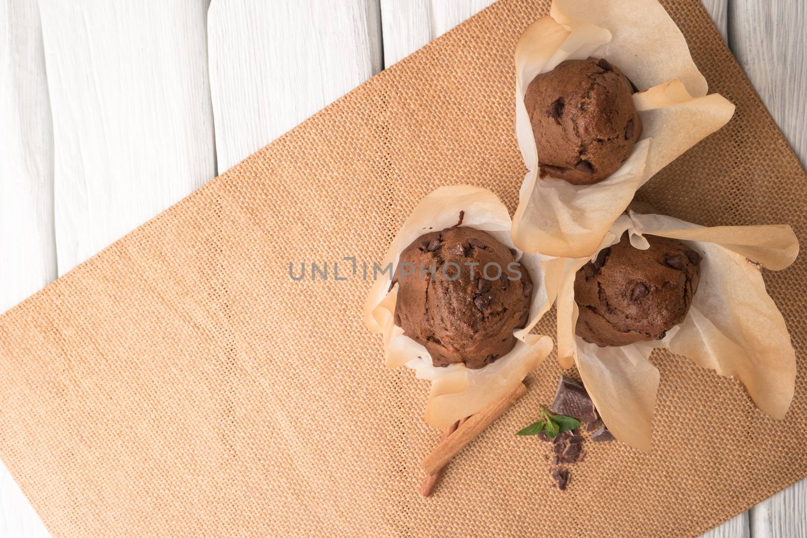 Chocolate muffins with chocolate slices in basket, cinnamom sticks and mint on placemat
