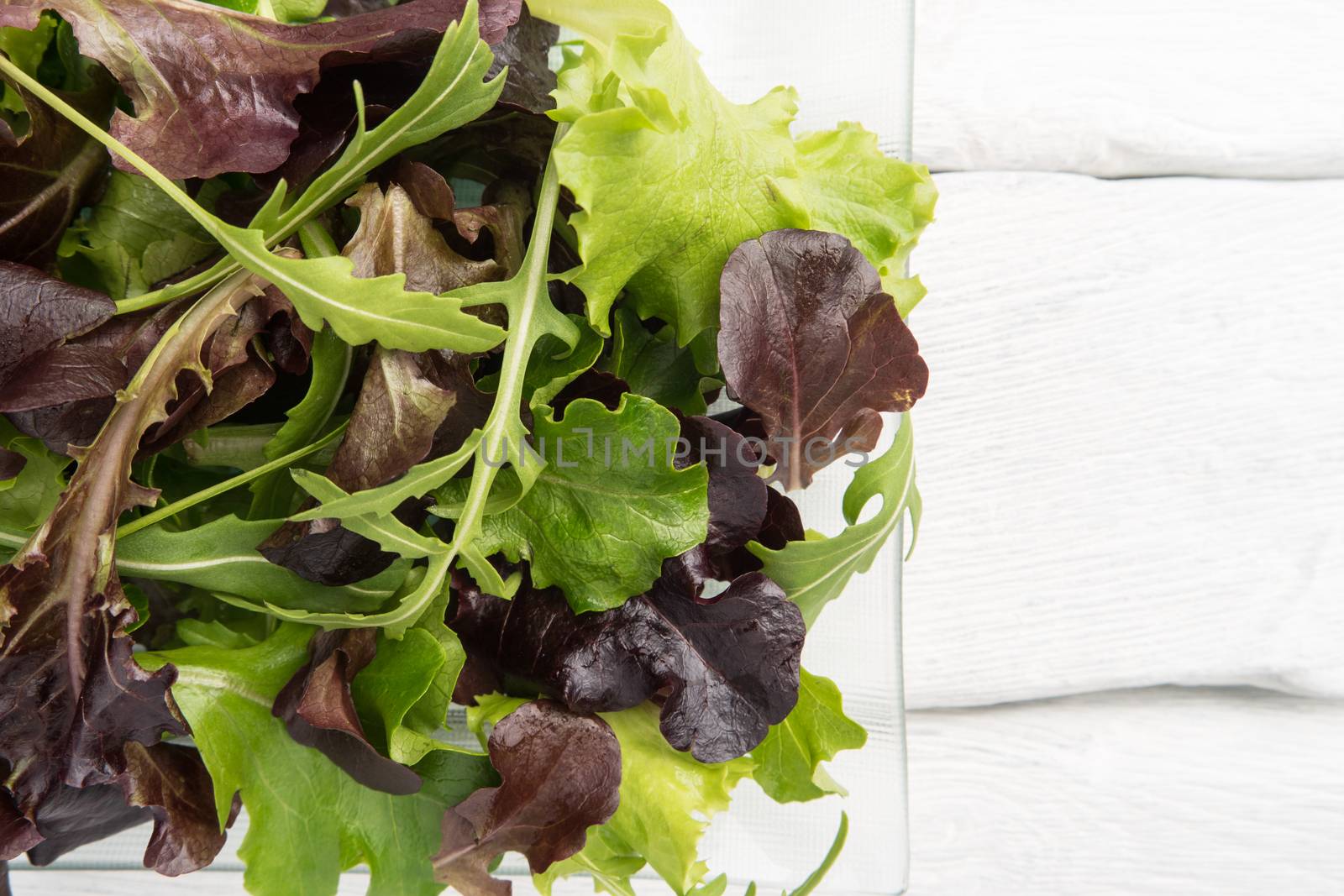 Fresh green salad with spinach, arugula, romaine and lettuce on plate. wood background