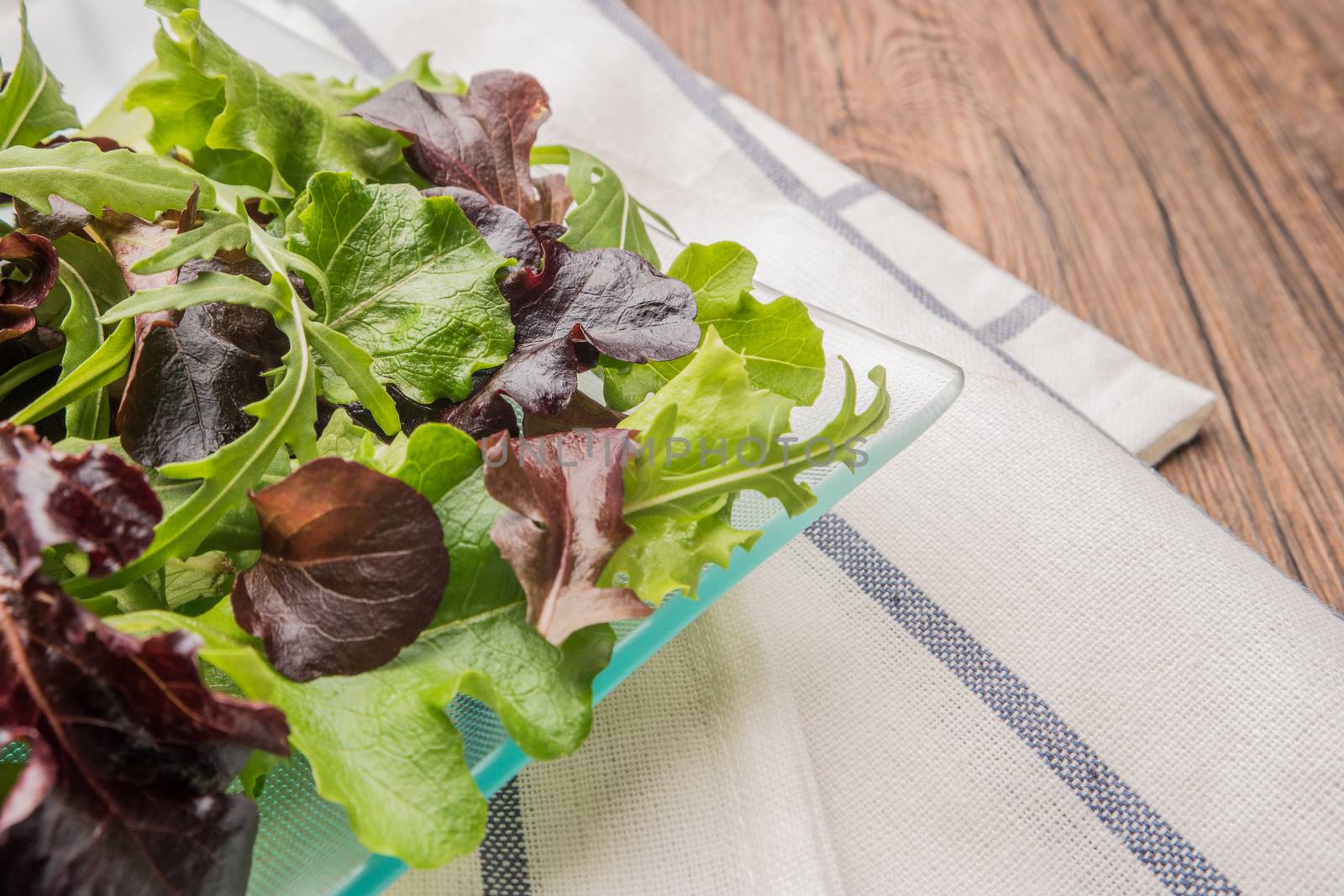 Fresh green salad with spinach, arugula, romaine and lettuce on plate. wood background