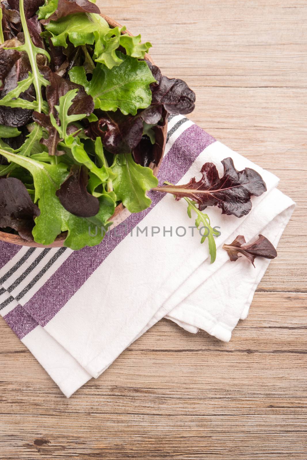 Fresh green salad with spinach, arugula, romaine and lettuce in a bowl on rustic wooden background