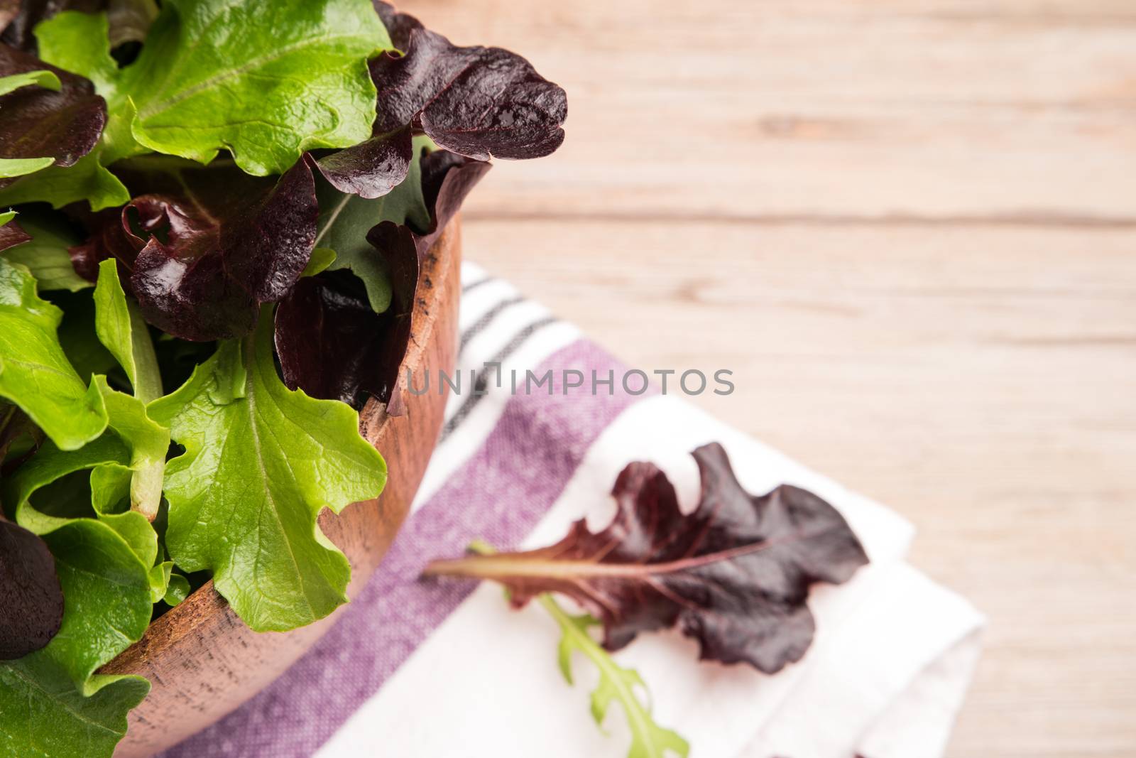 Fresh green salad with spinach, arugula, romaine and lettuce in a bowl on rustic wooden background