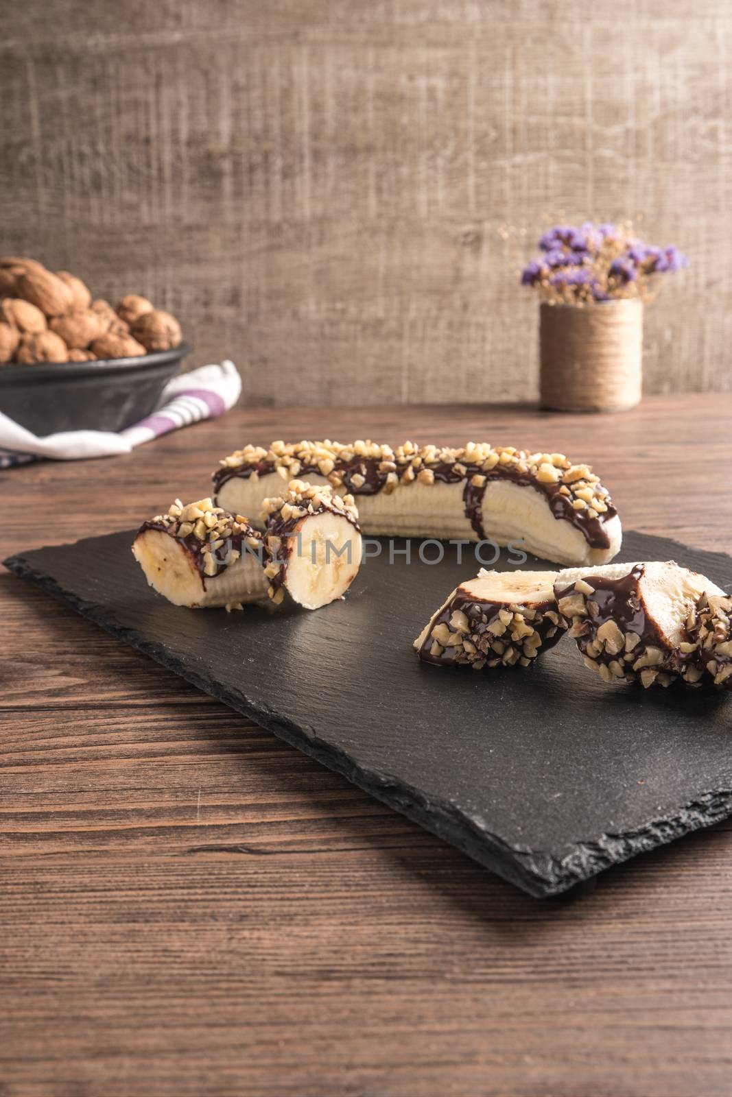Fresh banana with melted chocolate and nuts coverage on slate