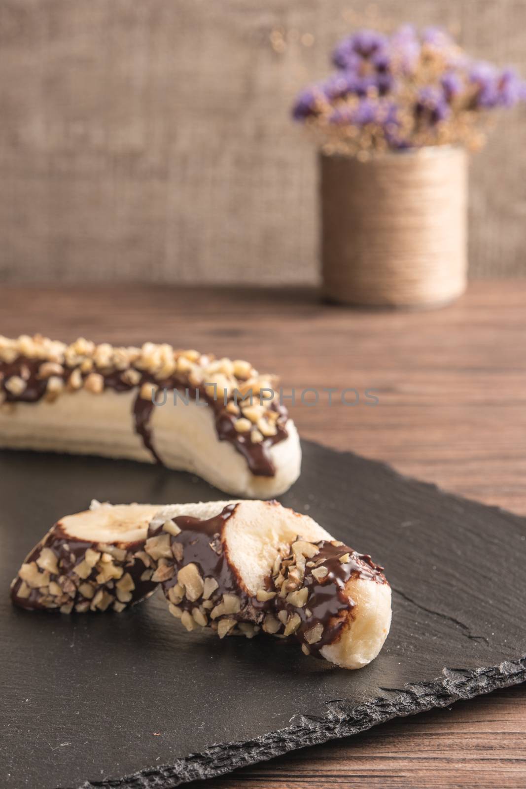 Fresh banana with melted chocolate and nuts coverage on slate