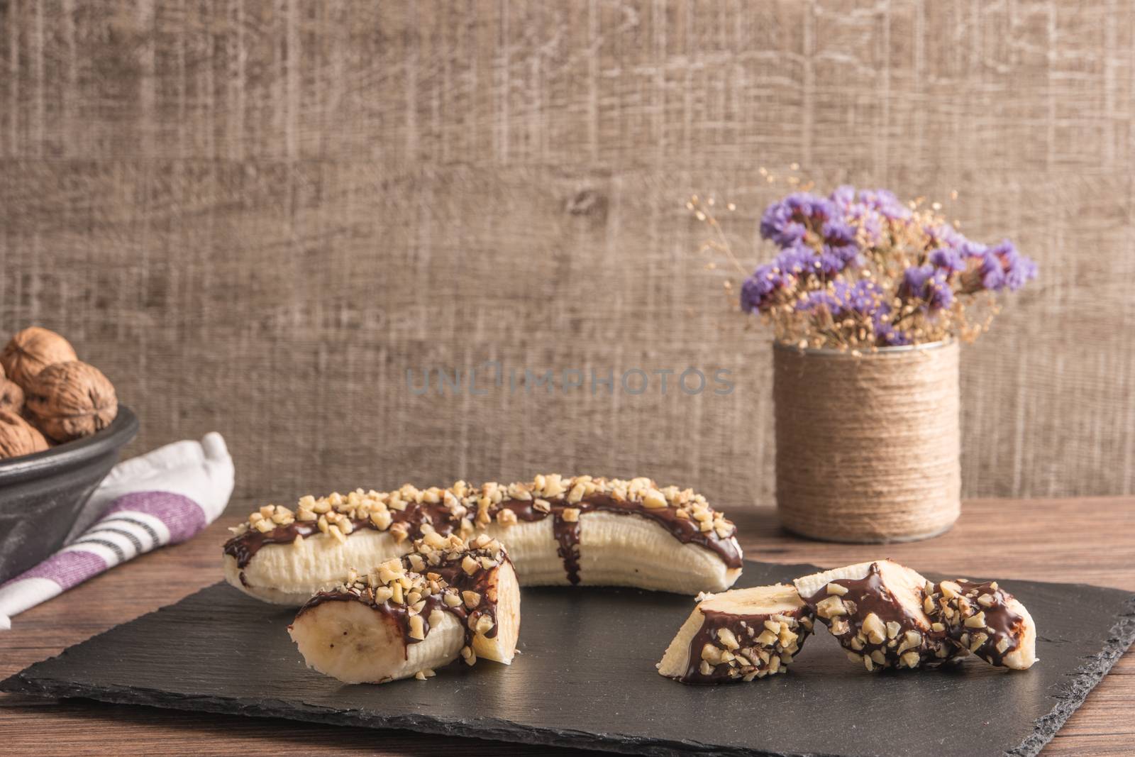 Fresh banana with melted chocolate and nuts coverage on slate