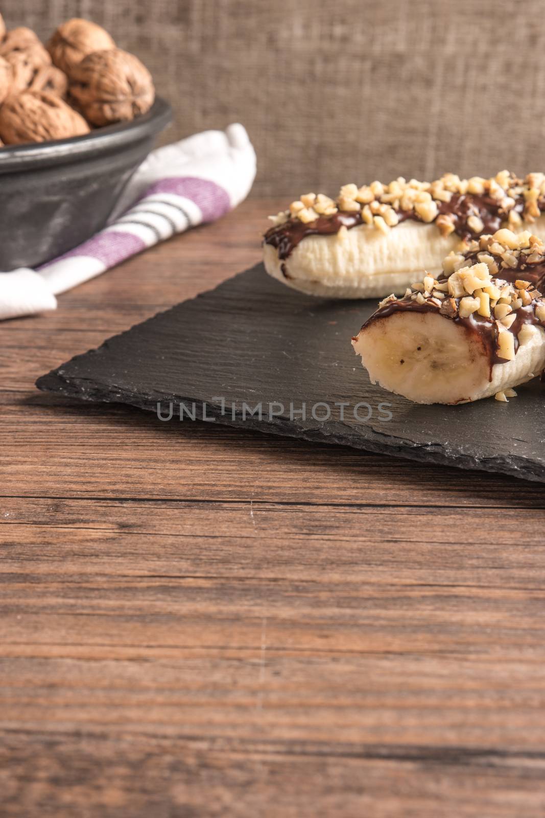 Fresh banana with melted chocolate and nuts coverage on slate