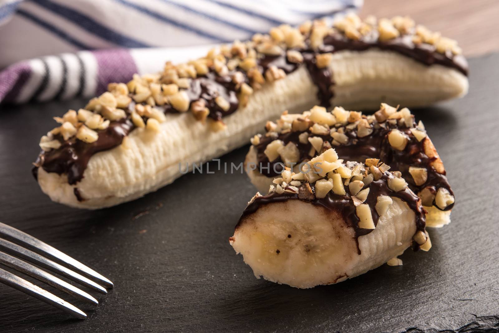 Fresh banana with melted chocolate and nuts coverage on slate