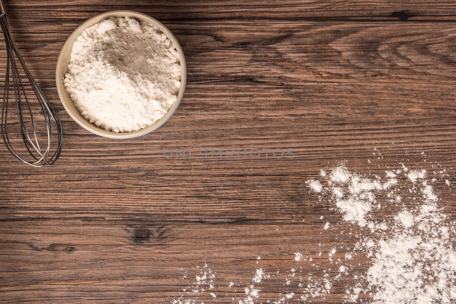 Flour in ceramic bowl and beater on the wooden table closeup. Top view with copy space