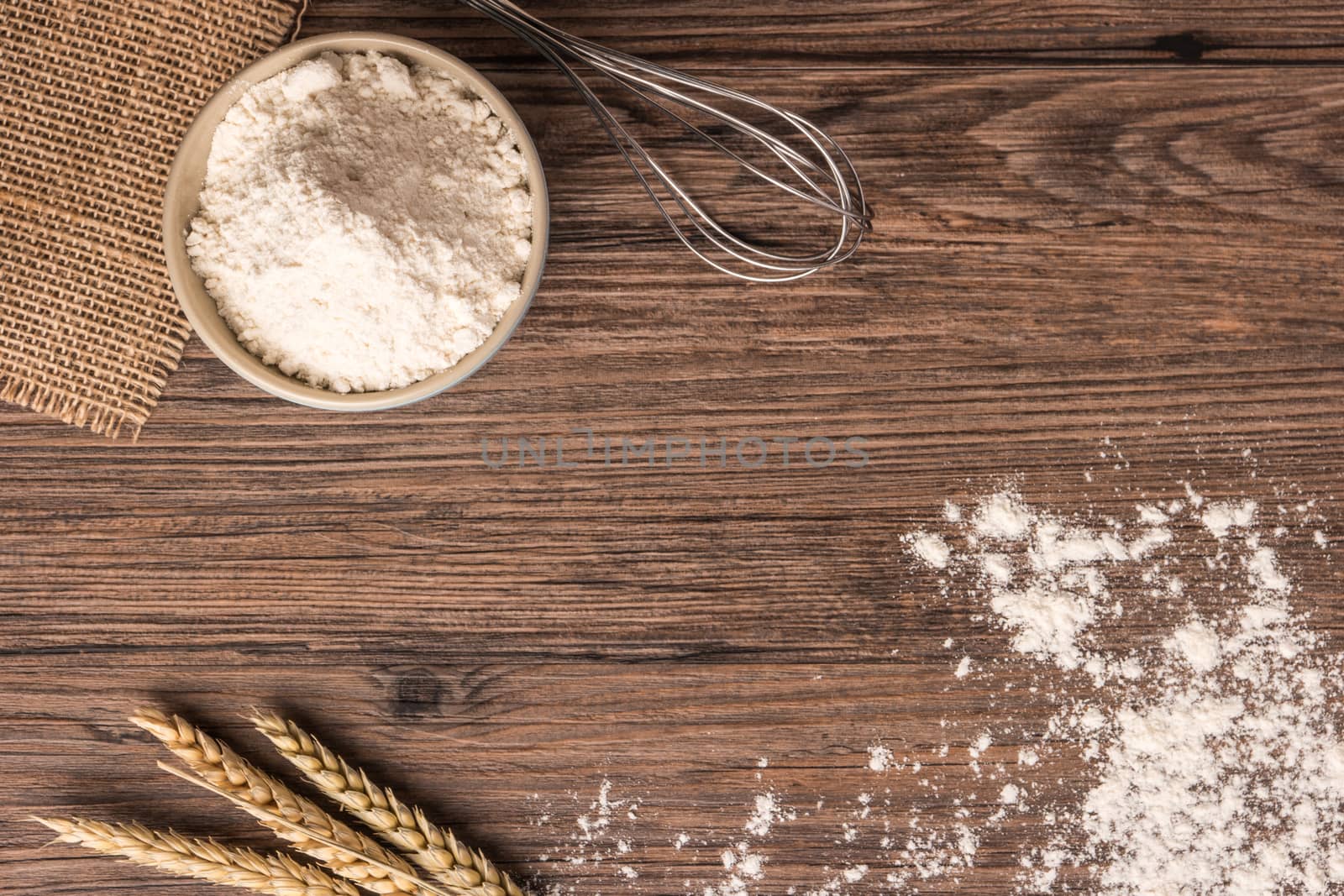 Flour in ceramic bowl with a handful with ears of wheat and beater on the wooden table closeup. Top view with copy space