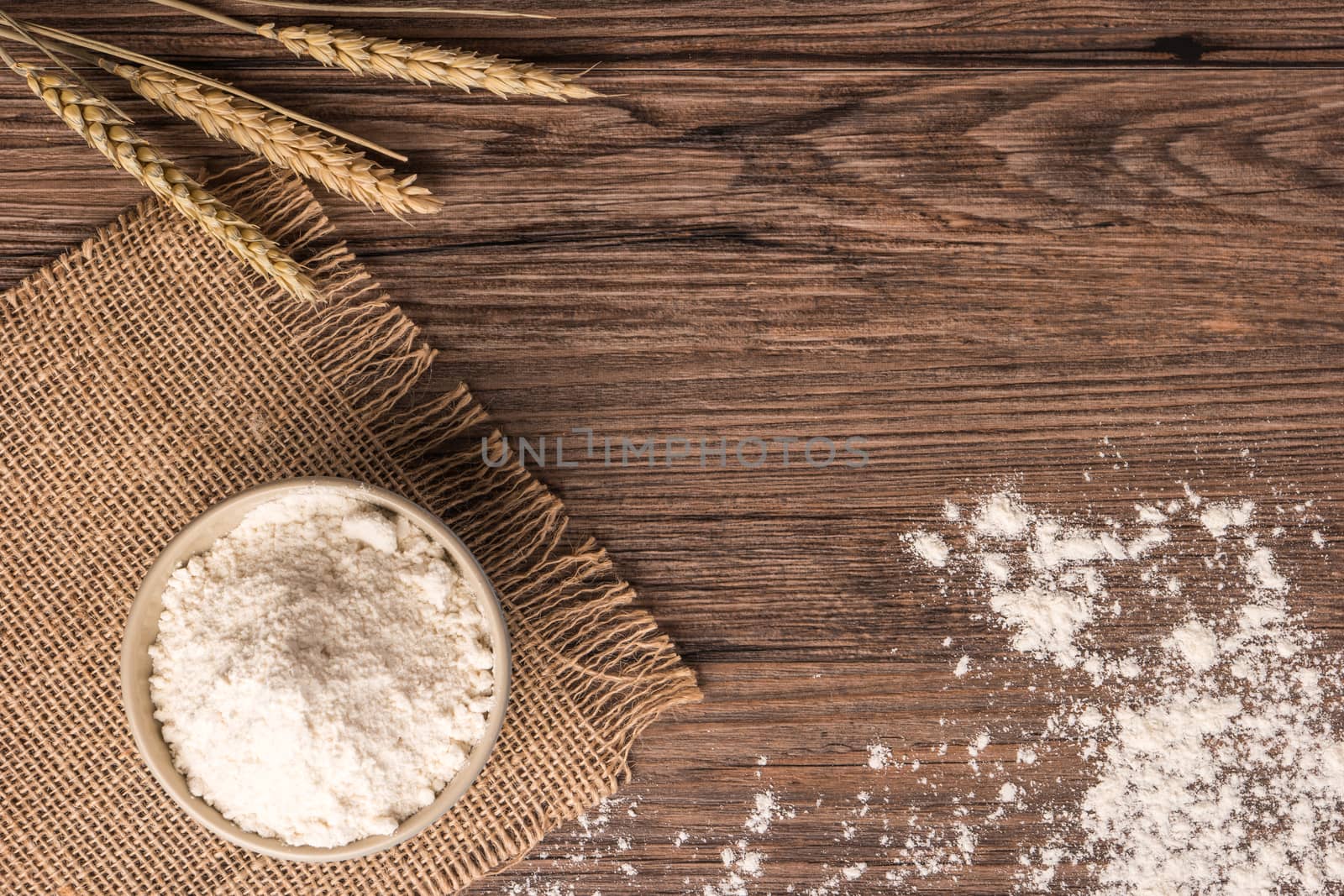 Flour in ceramic bowl with a handful with ears of wheat on the wooden table closeup. Top view with copy space