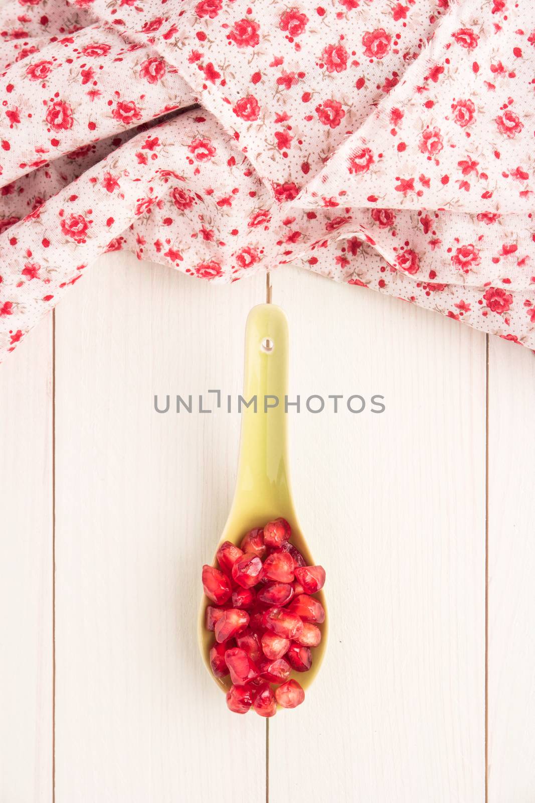 Seeds of red ripe peeled pomegranate on ceramic spoon. by AnaMarques