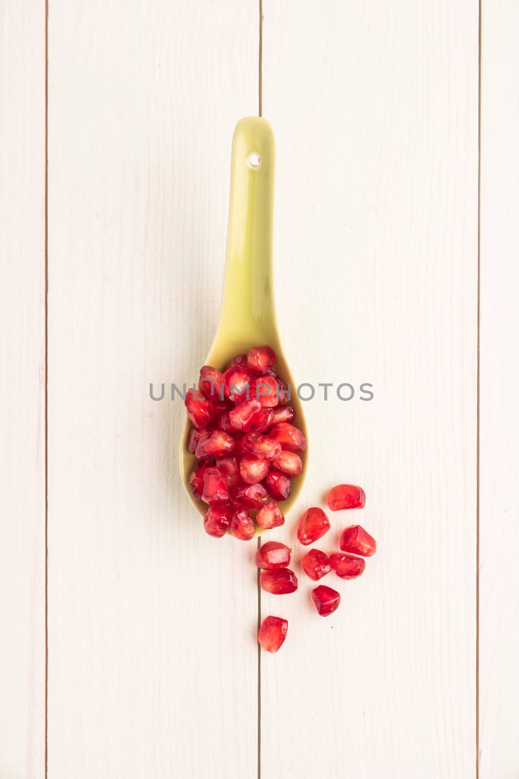 Seeds of red ripe peeled pomegranate on ceramic spoon. Rustic wood board background. Top view, copy space