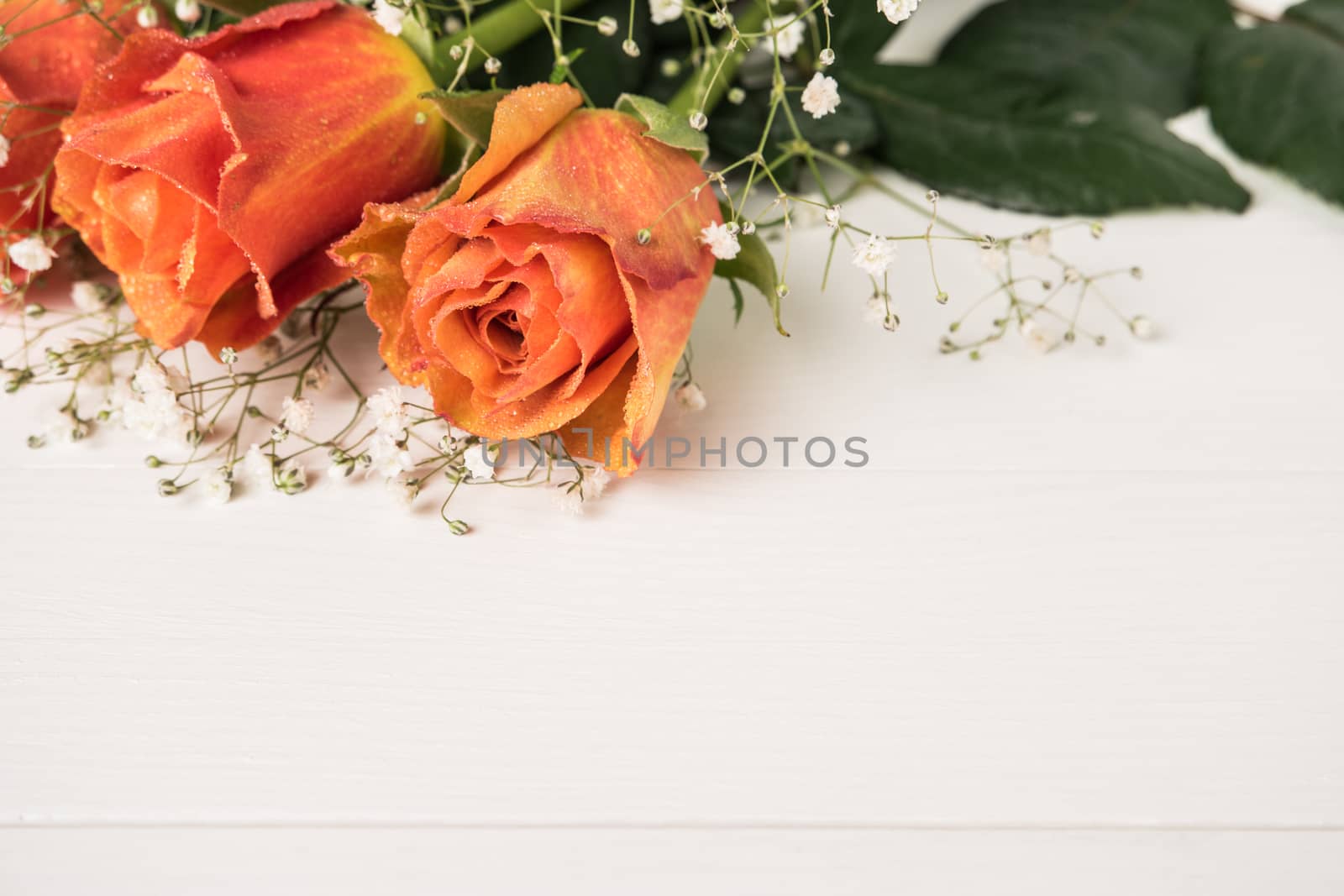 A bouquet of orange roses and gypsophila on wooden table. Copy space