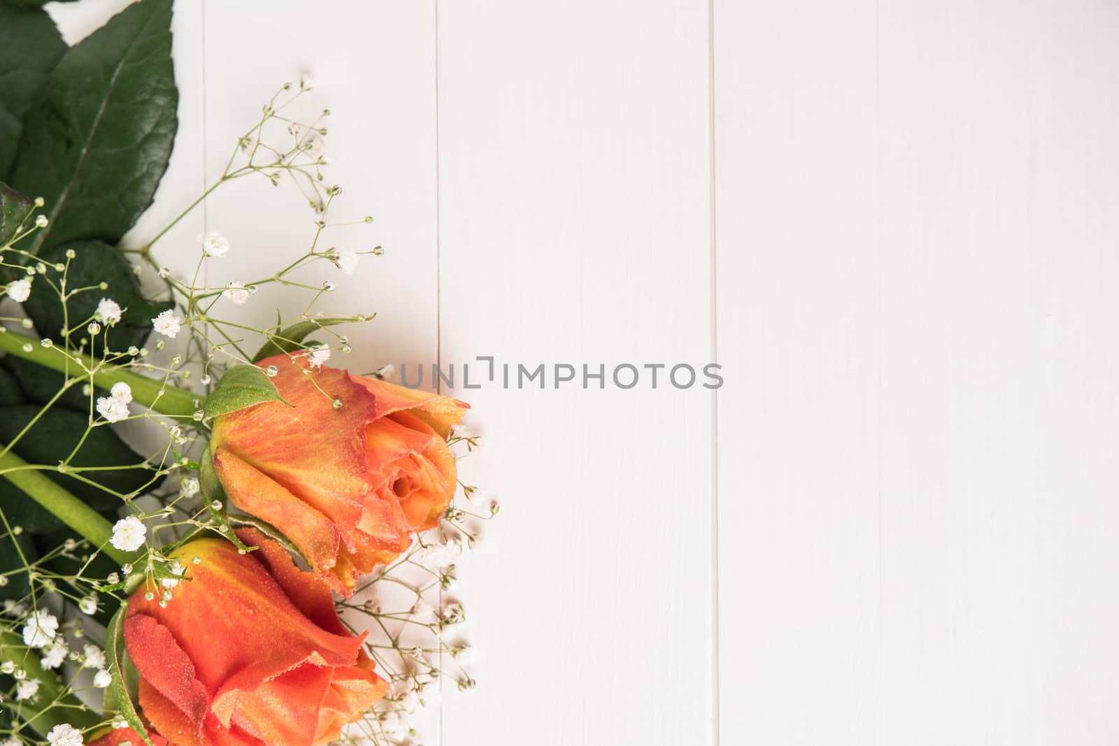 A bouquet of orange roses and gypsophila on wooden table. Copy space