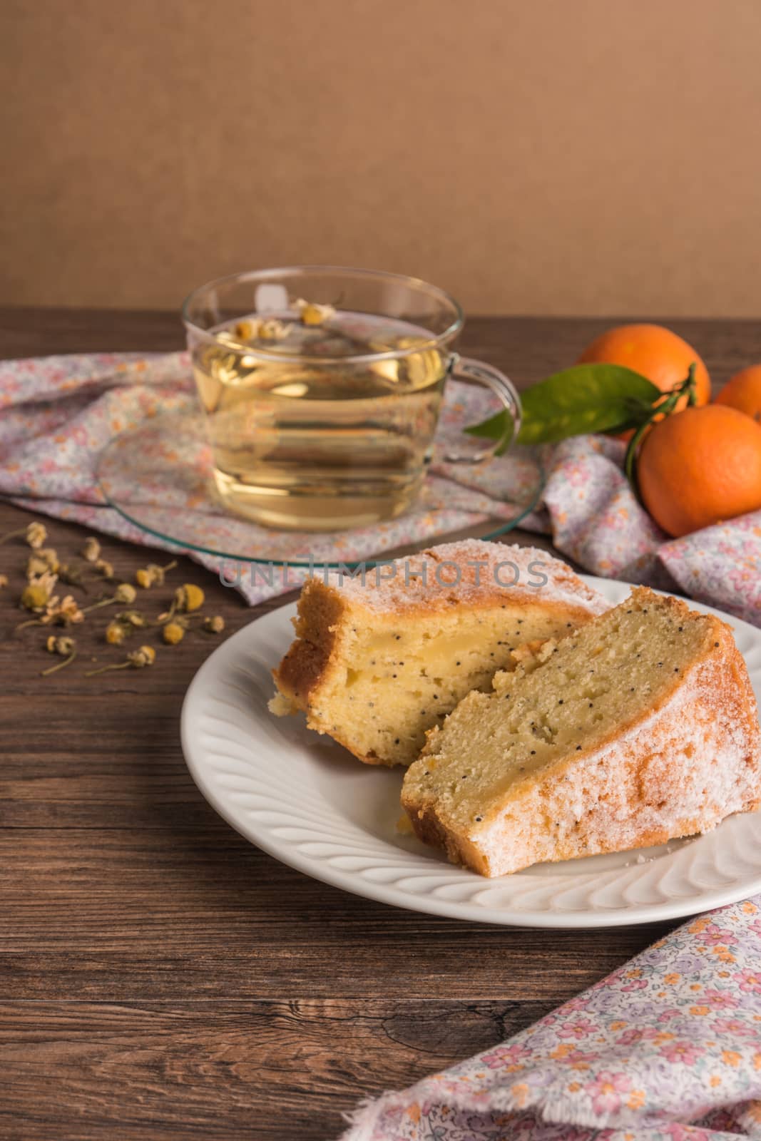 Slices of clementine cake with powdered sugar topping and cup of chamomile tea. Cake on a plate with fresh clementines on wooden board.