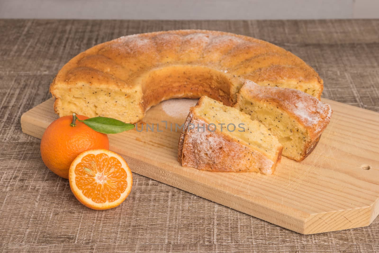 Slices of clementine cake with powdered sugar topping. Cake on a board with fresh clementines on wooden board.