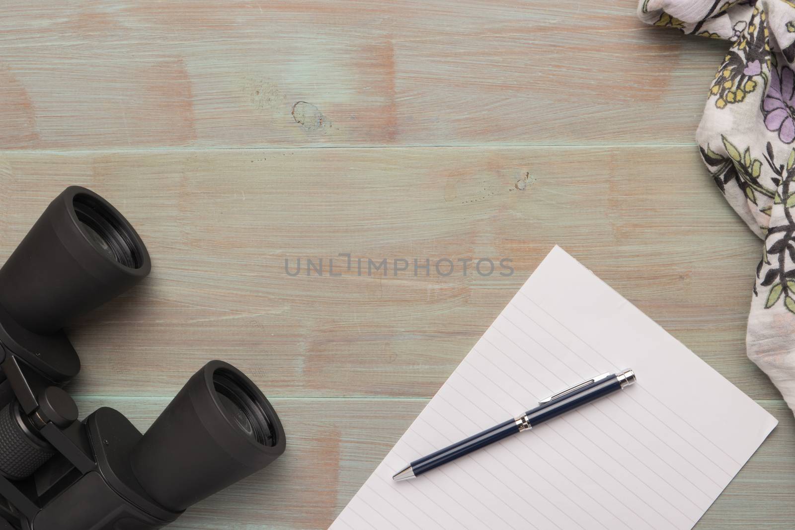 Travel, summer vacation, tourism and objects concept - close up binoculars, pen, paper and scarf on wooden table. Top view with copy space.