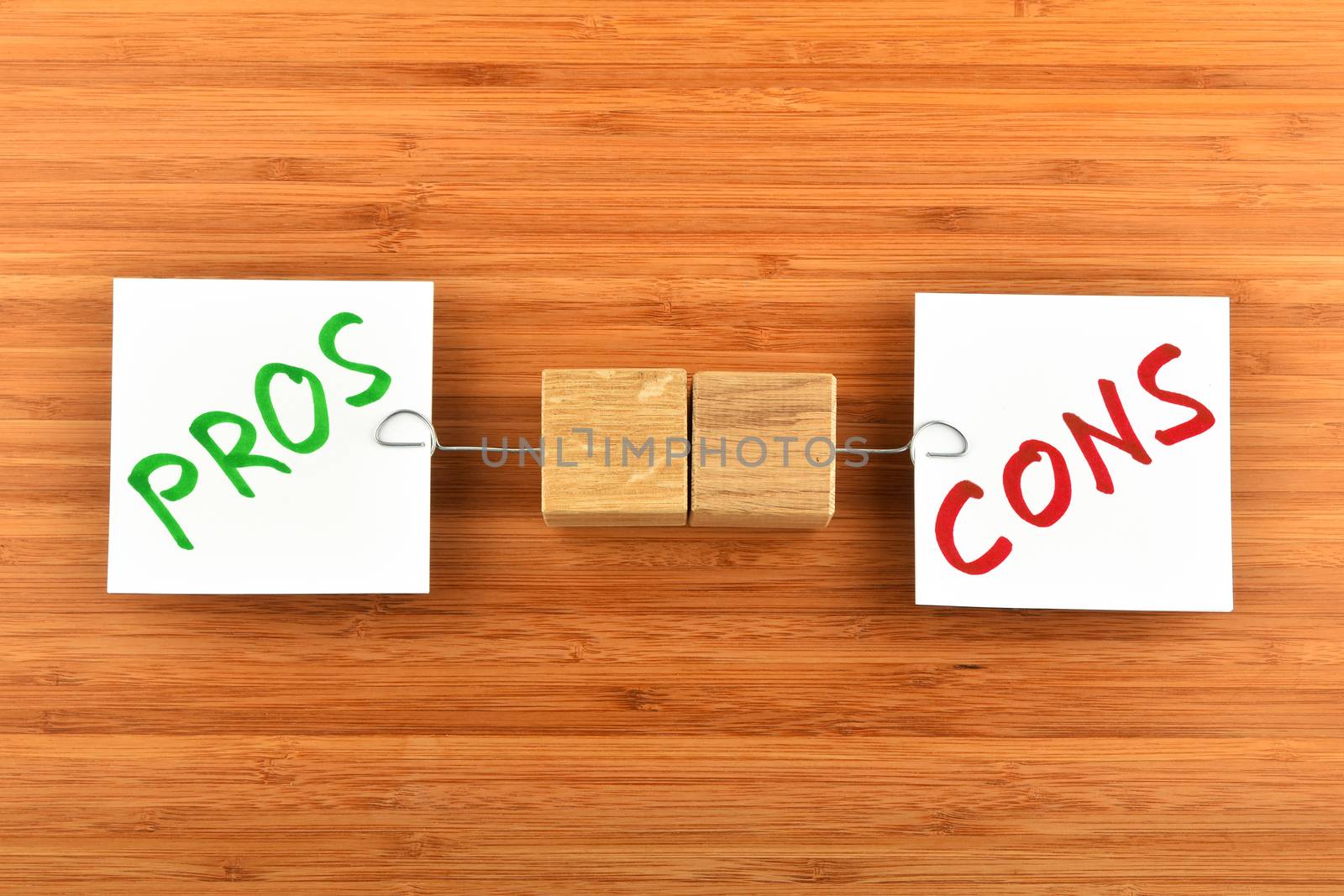 Choice, dilemma, two white paper notes with marker writter pros and cons words, wooden holders in different directions on bamboo wooden background for presentation